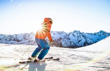 Professional skier athlete skiing at sunset on top of french alps ski resort - Winter vacation and sport concept with adventure guy on mountain top riding down the slope - Warm bright sunshine filter